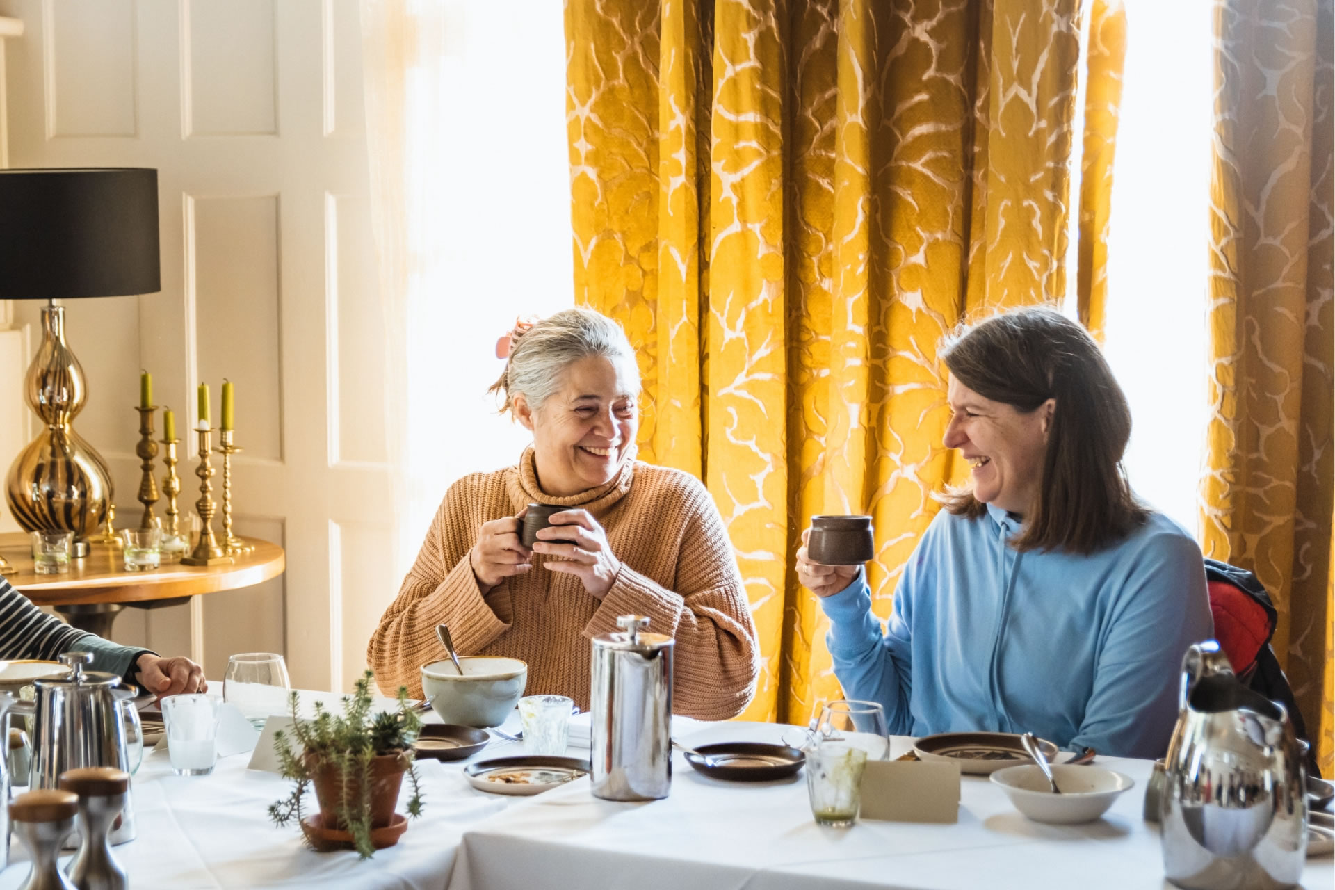 Two female clients smiling and talking over brunch at the Combe Grove