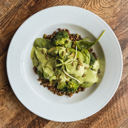 Green power bowl containing avocado, spinach and green lentils and pumpkin seeds flat lay